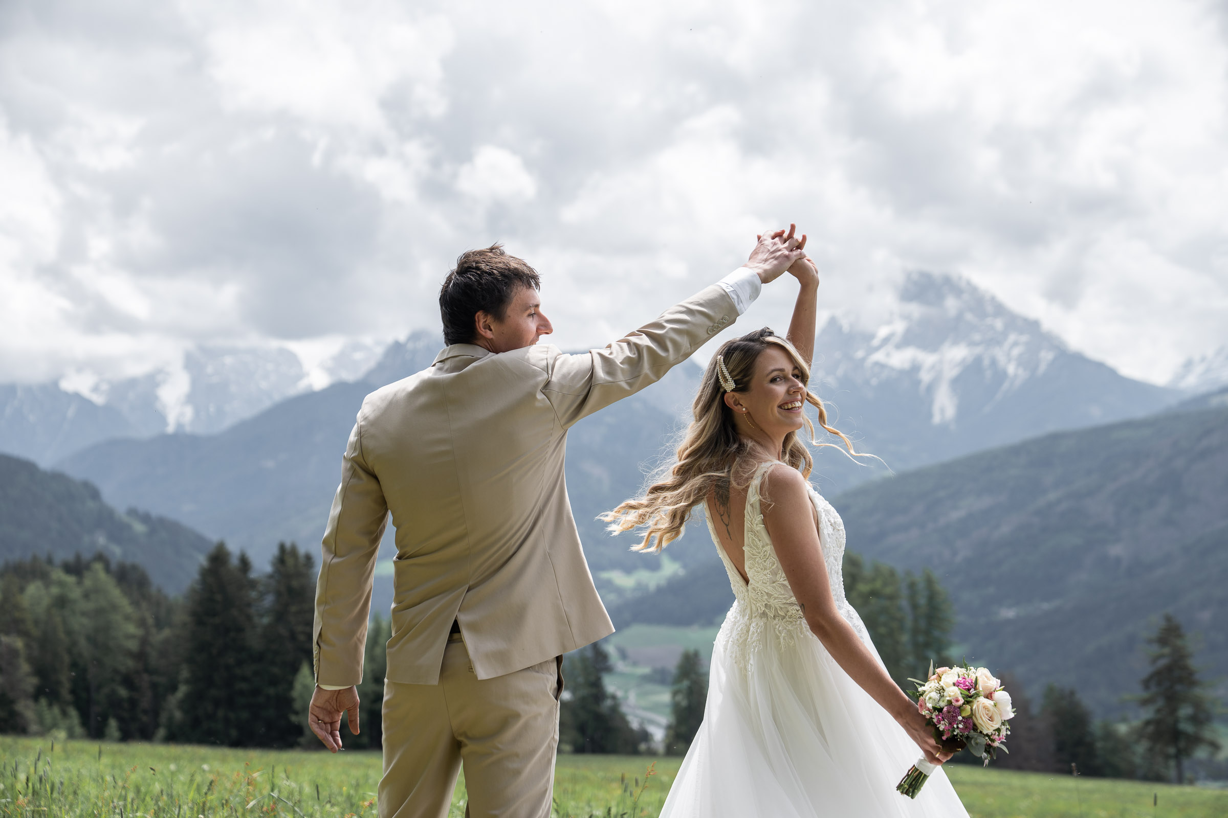 Groom twirling bride in a wildflower meadow, Dolomites behind