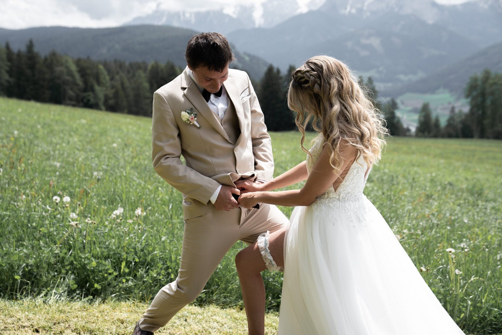 Lo sposo accovacciato aiuta la sposa nell’erba, dietro la valle e le montagne