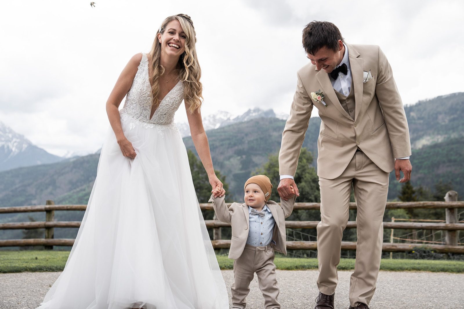 Gli sposi camminano tenendo per mano un bambino, dietro di loro le montagne