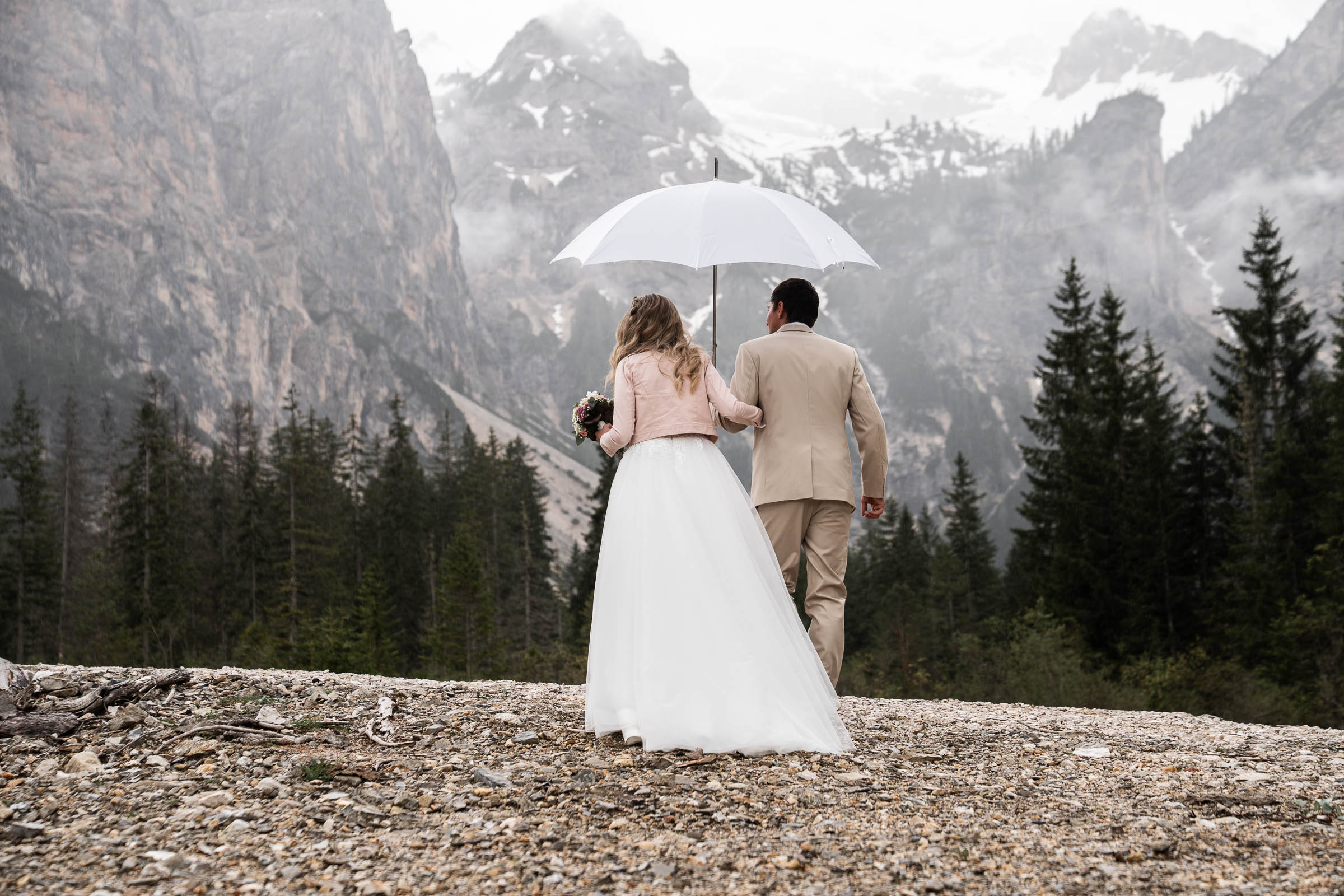 Couple beneath an umbrella walking toward the cloud-wrapped Dolomites