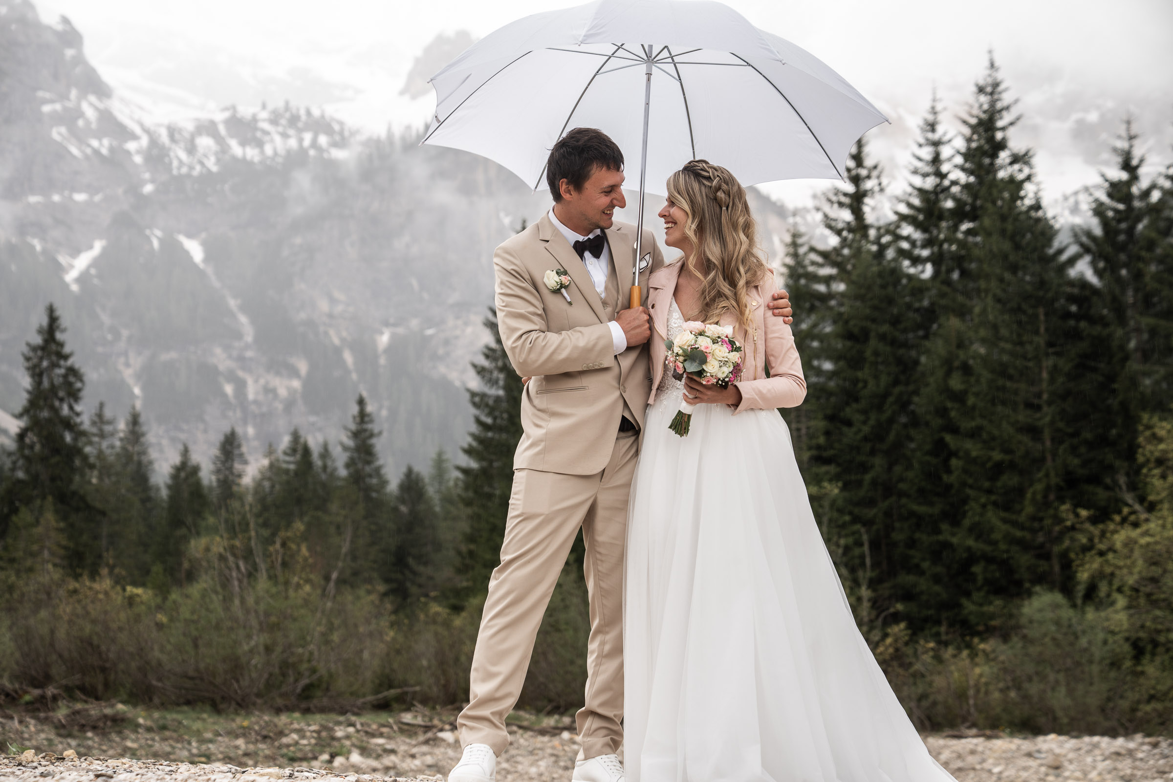 Bride and groom under a white umbrella, snow-capped peaks behind