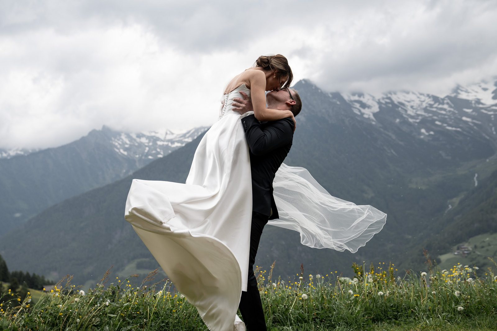 Lo sposo solleva la sposa, l’abito in volo, dietro le cime innevate