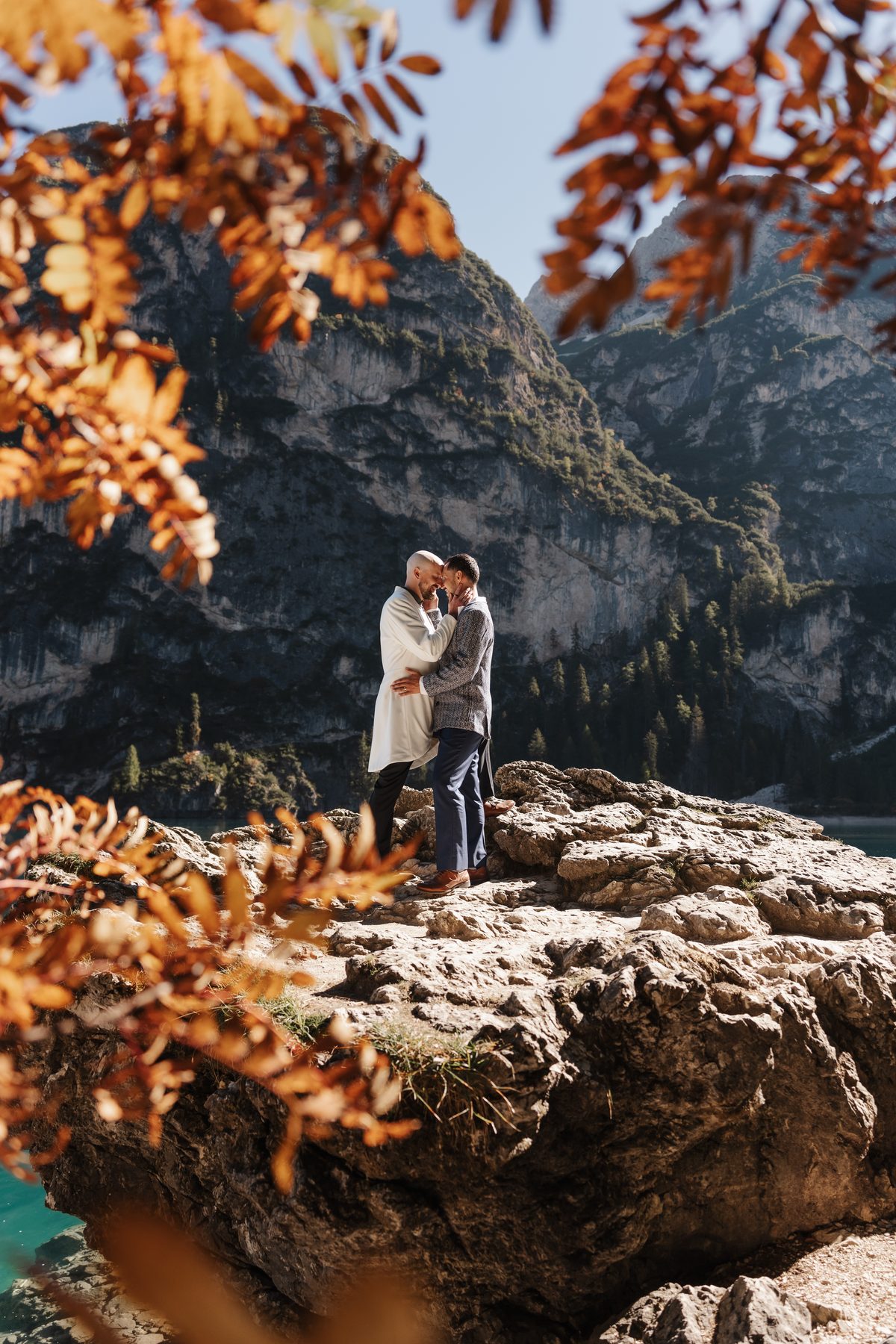 A kiss on a rock by the shore, orange autumn leaves in front
