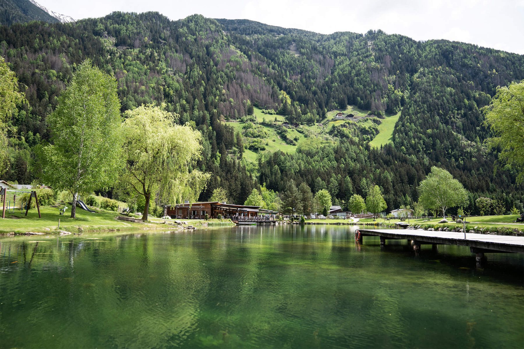 The lake by day with the jetty, the slopes of the Tauferer valley behind it